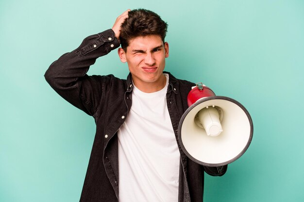 Young caucasian man holding a megaphone isolated on white background being shocked she has remembered important meeting