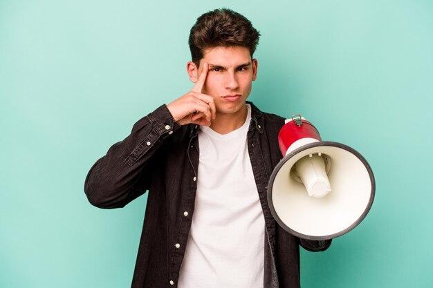 Young caucasian man holding a megaphone isolated on white background pointing temple with finger thinking focused on a task