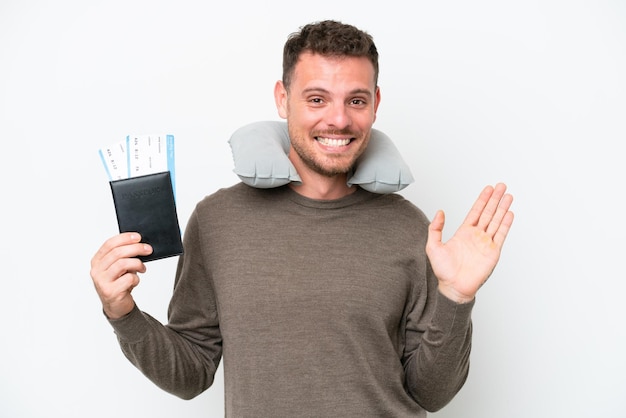 Young caucasian man holding a passport isolated on white background saluting with hand with happy expression