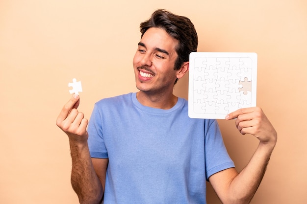 Young caucasian man holding a puzzle isolated on beige background