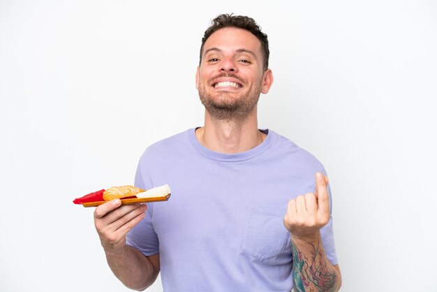 Young caucasian man holding sashimi isolated on white background making money gesture