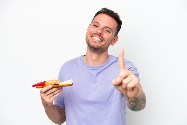 Young caucasian man holding sashimi isolated on white background showing and lifting a finger