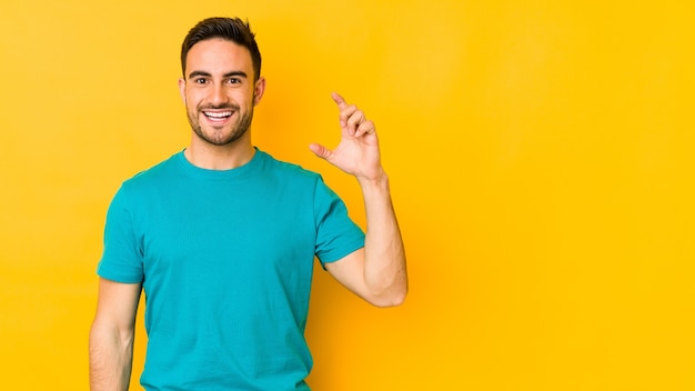 Young caucasian man holding something little with forefingers, smiling and confident.