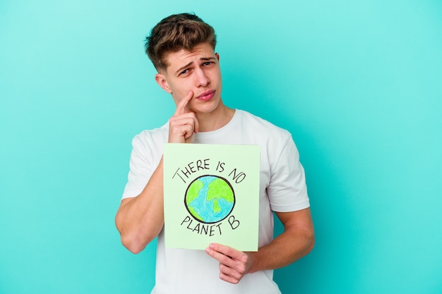 Young caucasian man holding a there is not planet b placard isolated on blue wall