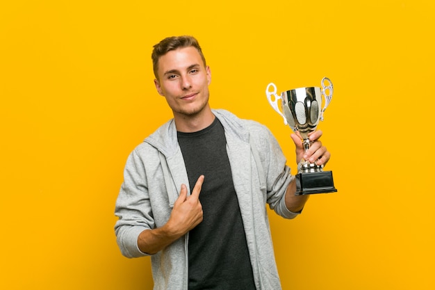 Photo young caucasian man holding a trophy pointing with finger at you as if inviting come closer.