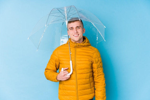 Young caucasian man holding an umbrella happy, smiling and cheerful.