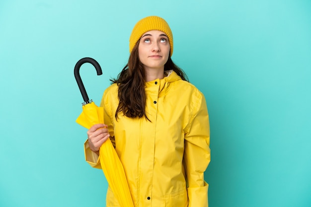 Young caucasian man holding an umbrella isolated on blue background and looking up