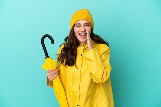 Young caucasian man holding an umbrella isolated on blue background shouting with mouth wide open