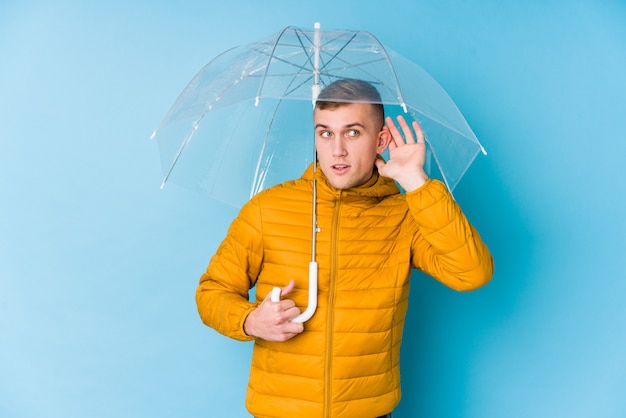 Young caucasian man holding an umbrella trying to listen a gossip.