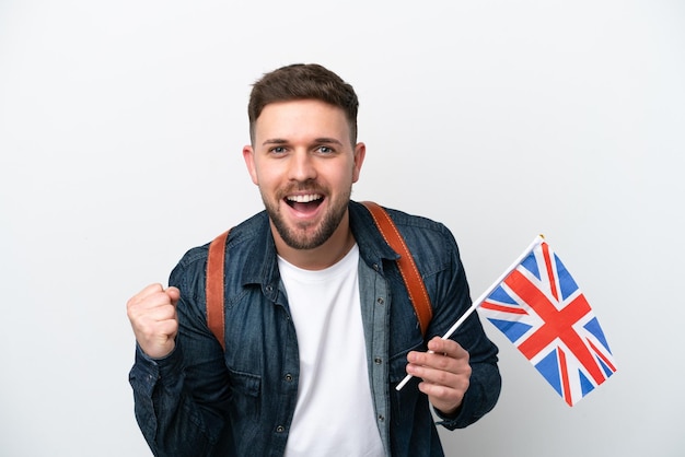 Young caucasian man holding an United Kingdom flag isolated on white background celebrating a victory in winner position