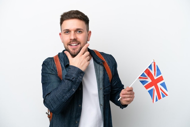 Young caucasian man holding an United Kingdom flag isolated on white background happy and smiling