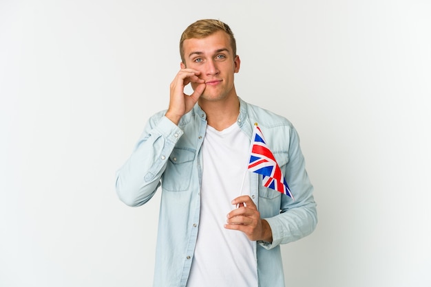 Young caucasian man holding a united kingdom flag isolated on white background with fingers on lips keeping a secret.