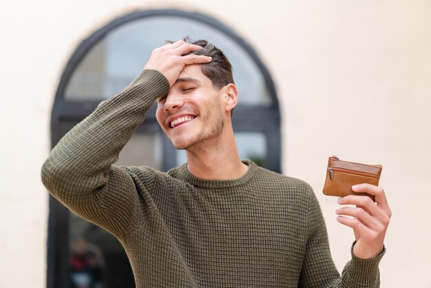 Young caucasian man holding a wallet at outdoors has realized something and intending the solution