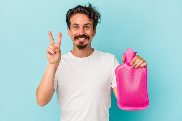 Young caucasian man holding a water bag isolated on blue background showing number two with fingers.