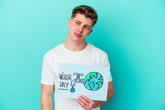 Young caucasian man holding a water day placard isolated on blue