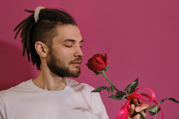 Young Caucasian man holds one red rose sniffs fragrance and smiles wants to give flower