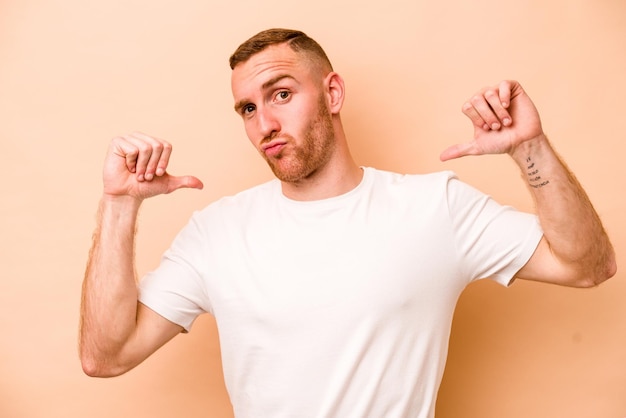 Young caucasian man isolated on beige background feels proud and self confident example to follow