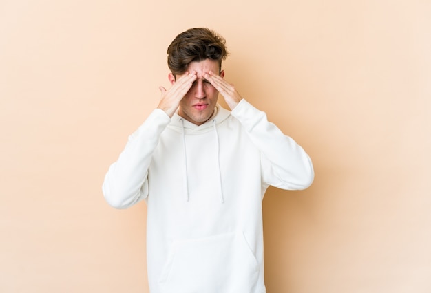 Young caucasian man isolated on beige background having a head ache, touching front of the face.