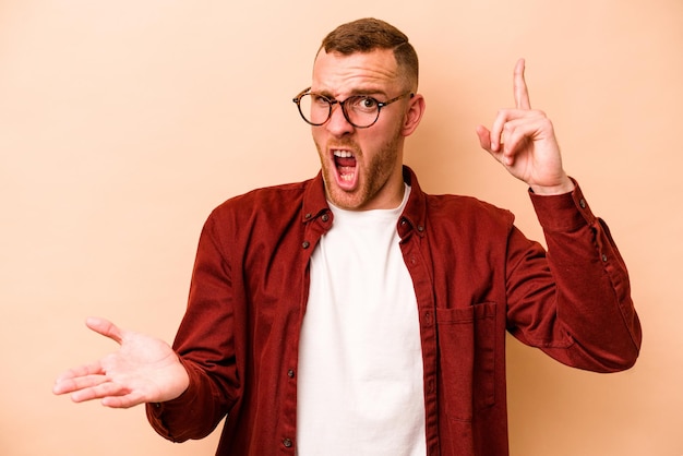 Young caucasian man isolated on beige background holding and showing a product on hand