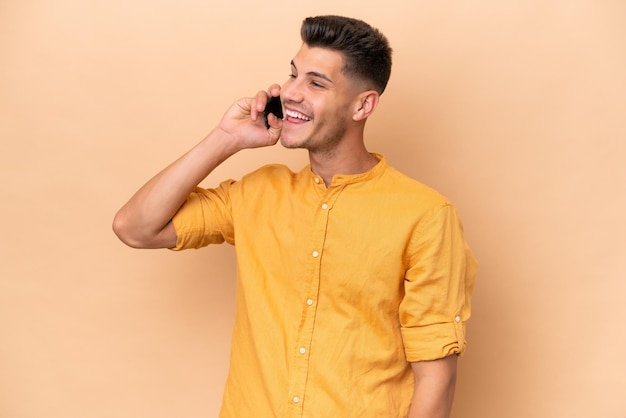 Young caucasian man isolated on beige background keeping a conversation with the mobile phone