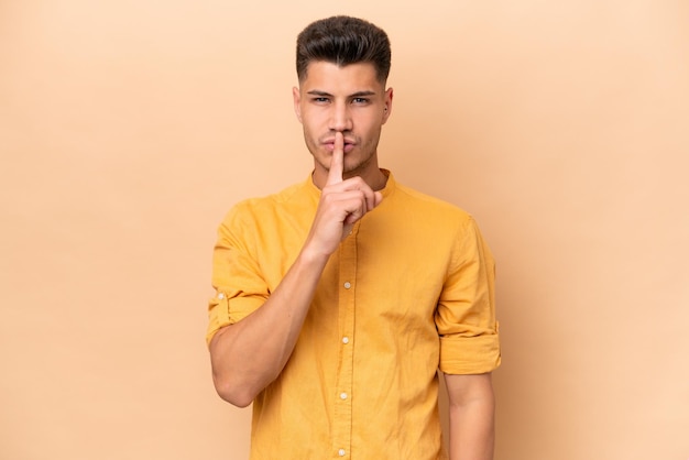 Young caucasian man isolated on beige background showing a sign of silence gesture putting finger in mouth