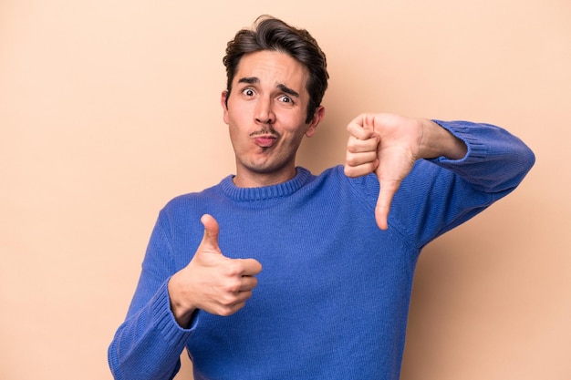 Young caucasian man isolated on beige background showing thumbs up and thumbs down, difficult choose concept