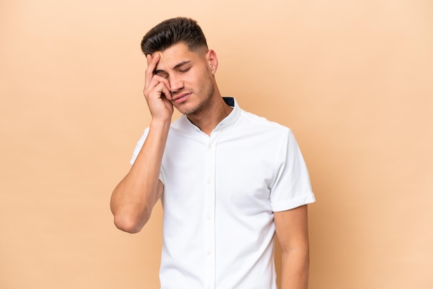 Young caucasian man isolated on beige background with headache