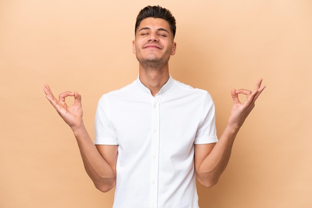 Young caucasian man isolated on beige background in zen pose