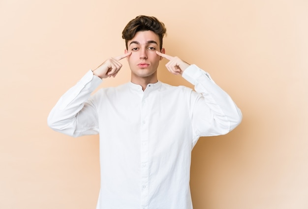 Young caucasian man isolated on beige wall focused on a task, keeping forefingers pointing head.