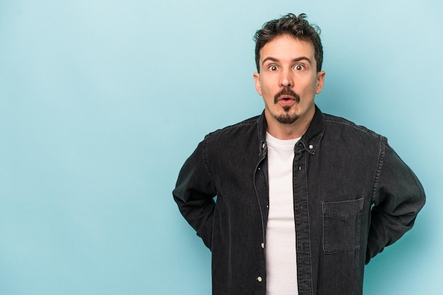 Young caucasian man isolated on blue background being shocked because of something she has seen.