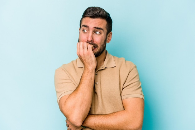 Young caucasian man isolated on blue background biting fingernails nervous and very anxious