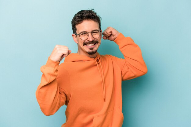 Young caucasian man isolated on blue background celebrating a special day, jumps and raise arms with energy.