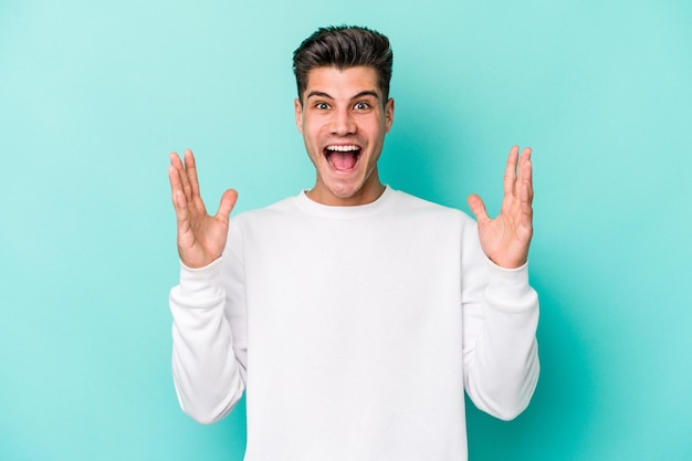 Young caucasian man isolated on blue background celebrating a victory or success, he is surprised and shocked.