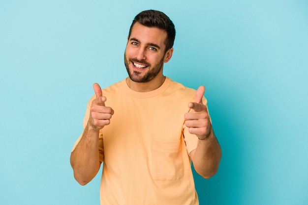 Young caucasian man isolated on blue background cheerful smiles pointing to front.