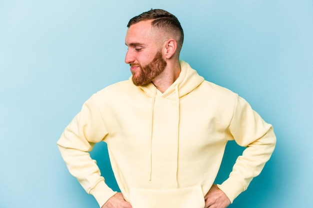 Young caucasian man isolated on blue background dreaming of achieving goals and purposes