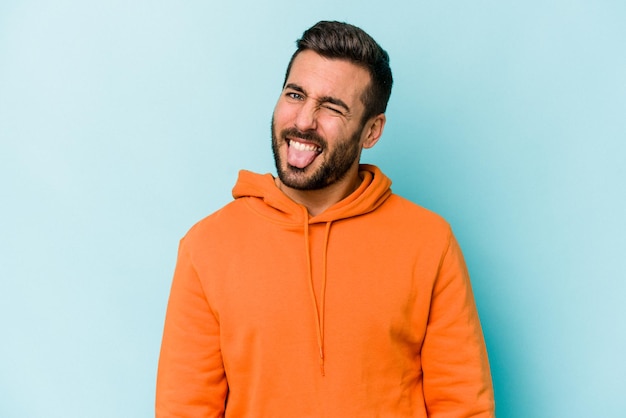 Young caucasian man isolated on blue background funny and friendly sticking out tongue