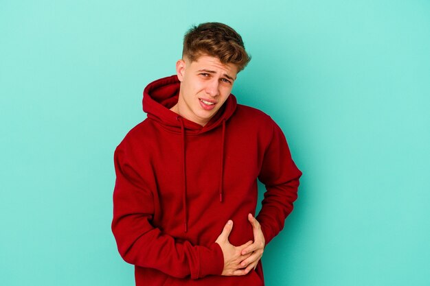 Young caucasian man isolated on blue background having a liver pain, stomach ache.