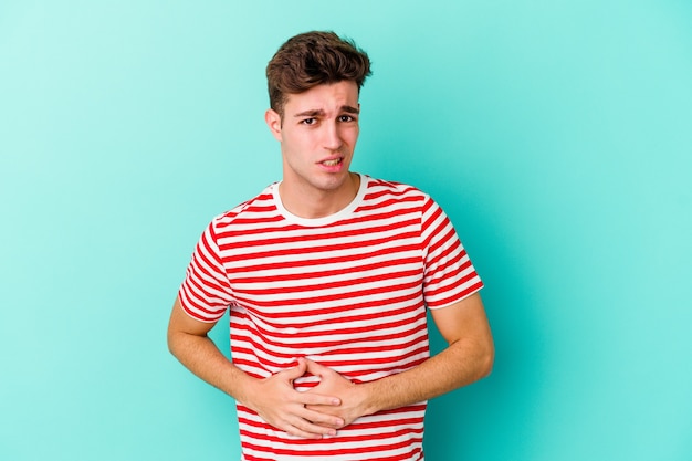 Young caucasian man isolated on blue background having a liver pain, stomach ache.