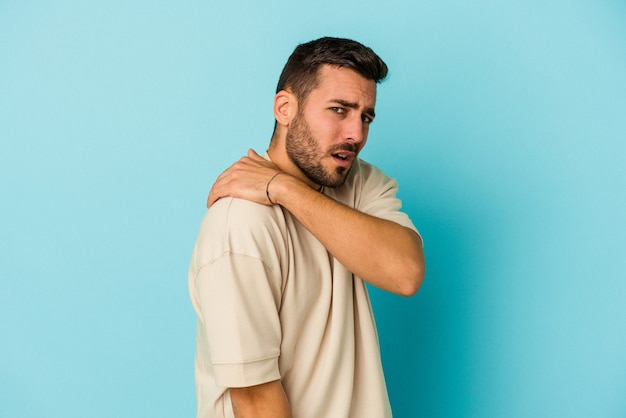 Young caucasian man isolated on blue background having a shoulder pain.