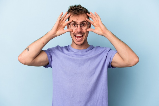 Young caucasian man isolated on blue background keeping eyes opened to find a success opportunity.