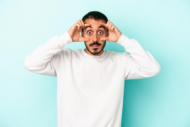 Young caucasian man isolated on blue background keeping eyes opened to find a success opportunity