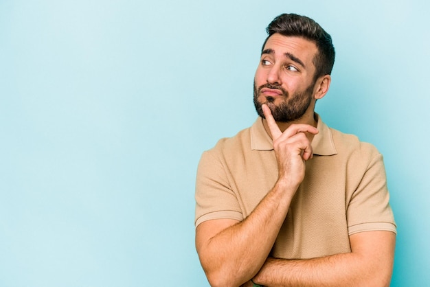 Young caucasian man isolated on blue background looking sideways with doubtful and skeptical expression