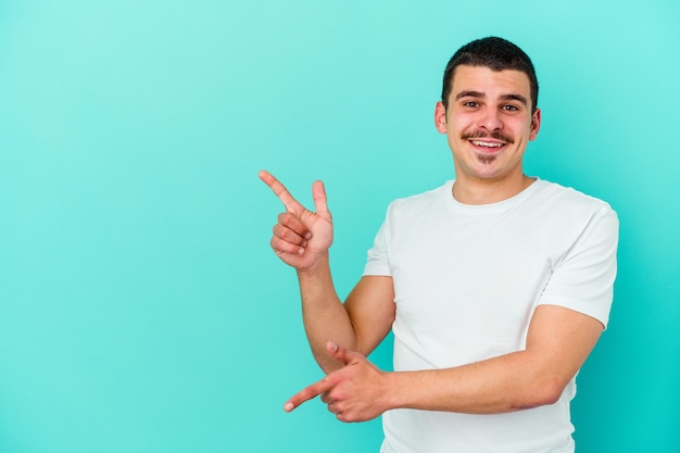 Young caucasian man isolated on blue background pointing with forefingers to a copy space, expressing excitement and desire.