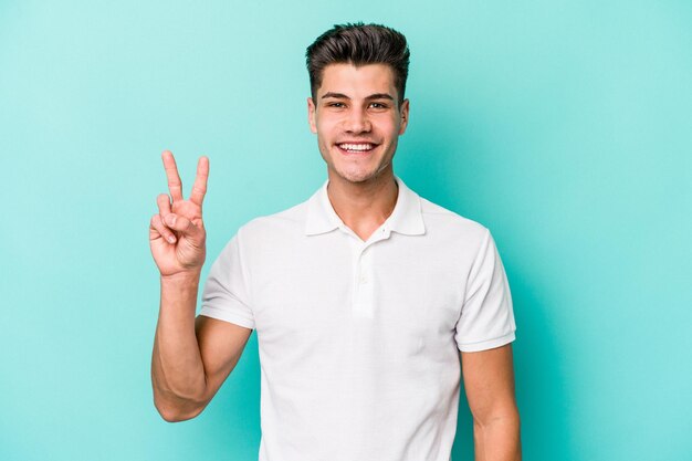 Young caucasian man isolated on blue background showing victory sign and smiling broadly