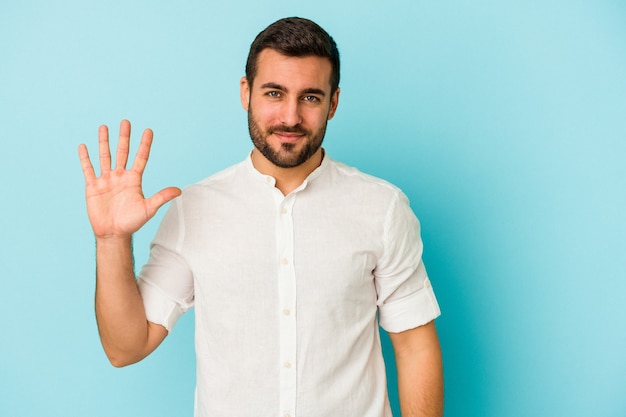 Young caucasian man isolated on blue background smiling cheerful showing number five with fingers.