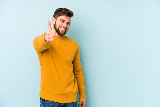 Young caucasian man isolated on blue background smiling and raising thumb up