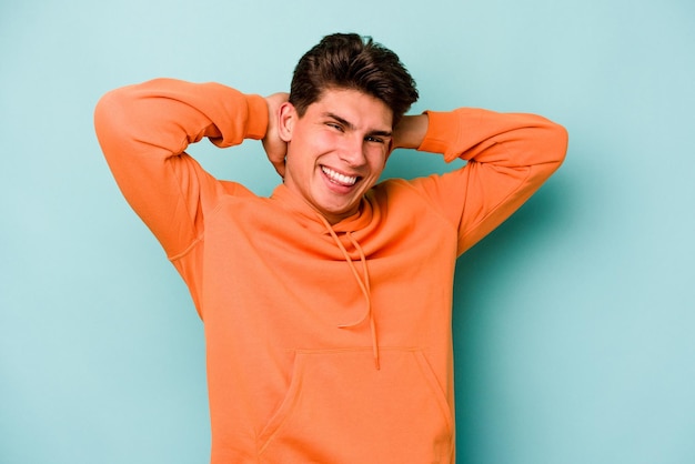 Young caucasian man isolated on blue background stretching arms relaxed position