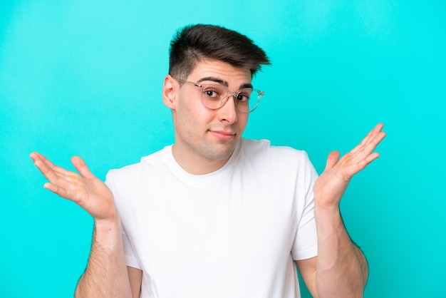 Young caucasian man isolated on blue background With glasses and having doubts