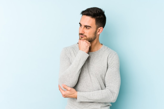 Young caucasian man isolated on blue looking sideways with doubtful and skeptical expression.