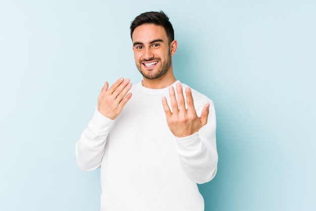 Young caucasian man isolated on blue pointing with finger at you as if inviting come closer.